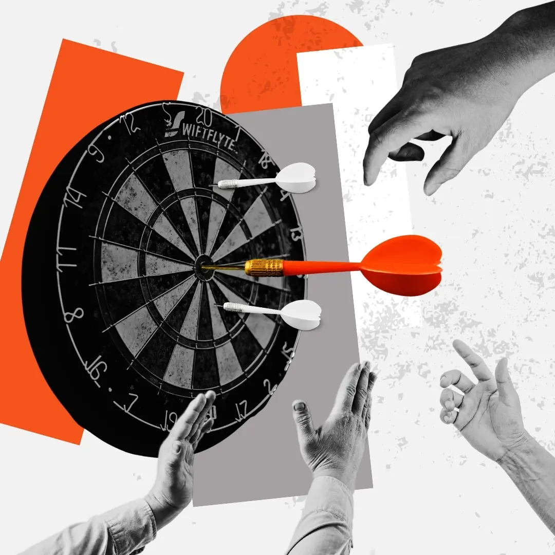 Hands reaching toward a dartboard where a large orange dart hits the bullseye